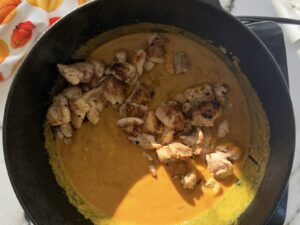 orange pumpkin curry in a cast iron pot with seared cubed chicken pieces on top.