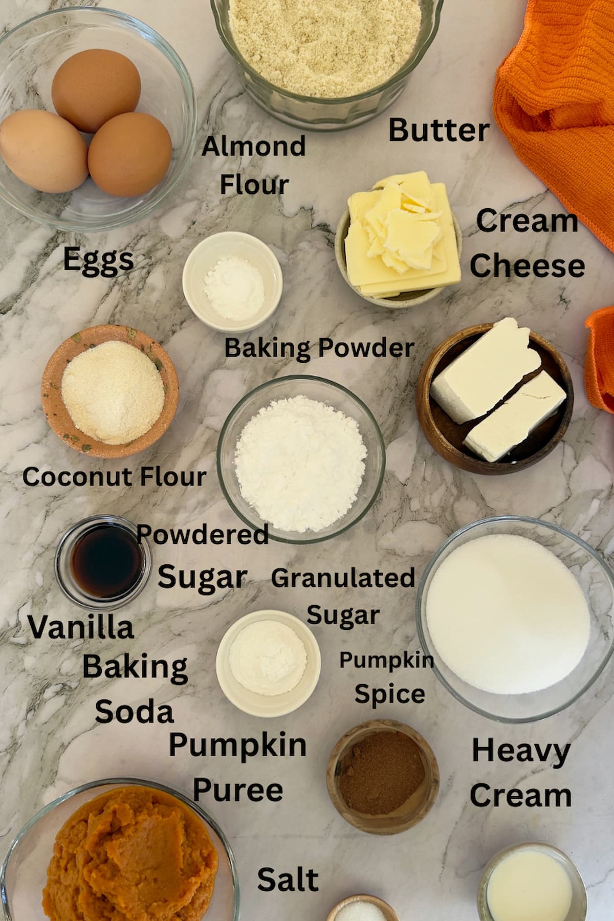 ingredients for pumpkin bread with cream cheese frosting laid out in separate bowls - eggs, almond flour, butter, cream cheese, baking powder, baking soda, salt, heavy cream, coconut flour, vanilla, powdered sugar, granulated sugar, pumpkin puree, pumpkin spice.
