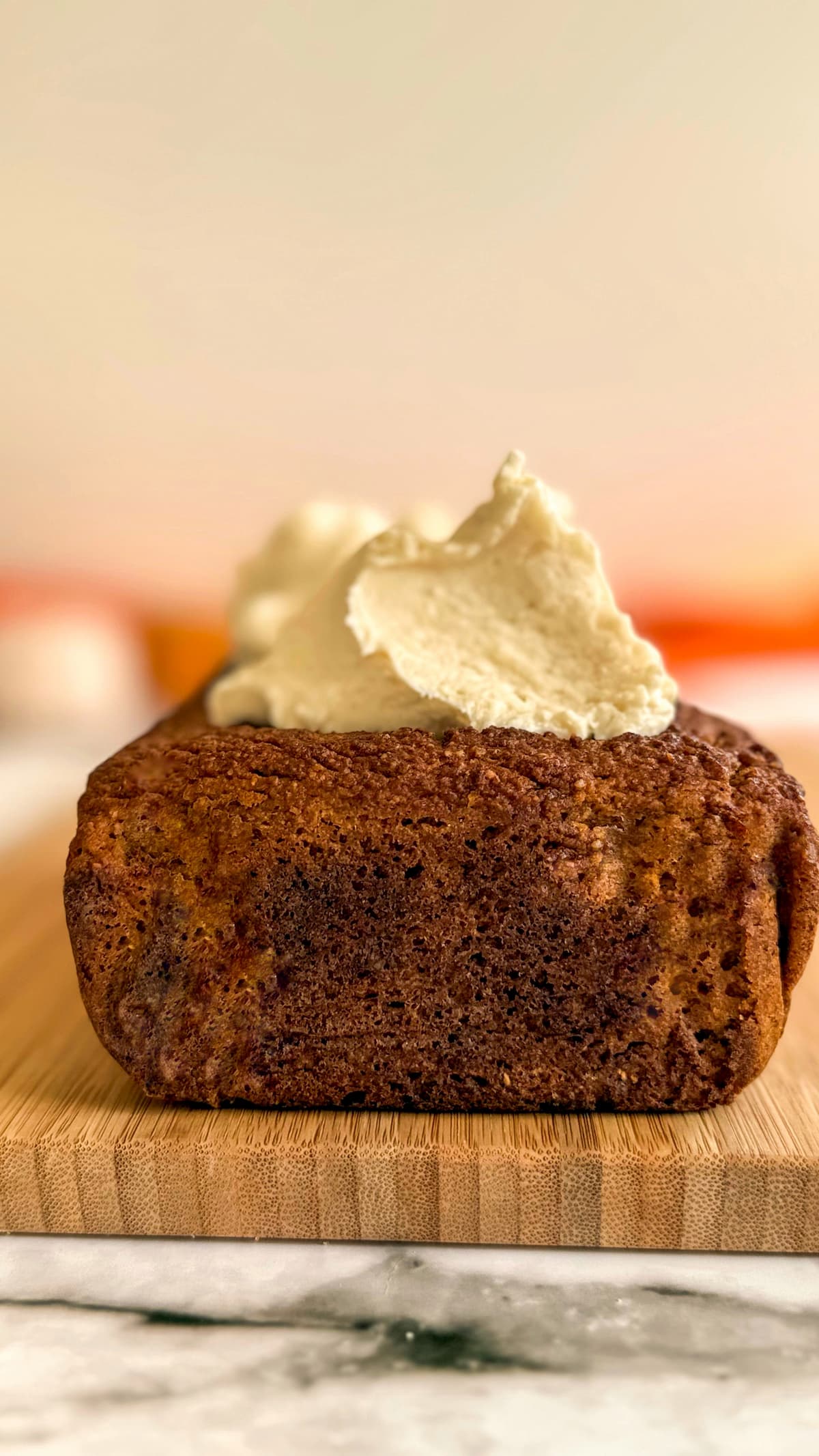 a pumpkin loaf on a cutting board topped with a few dollops of cream cheese frosting.