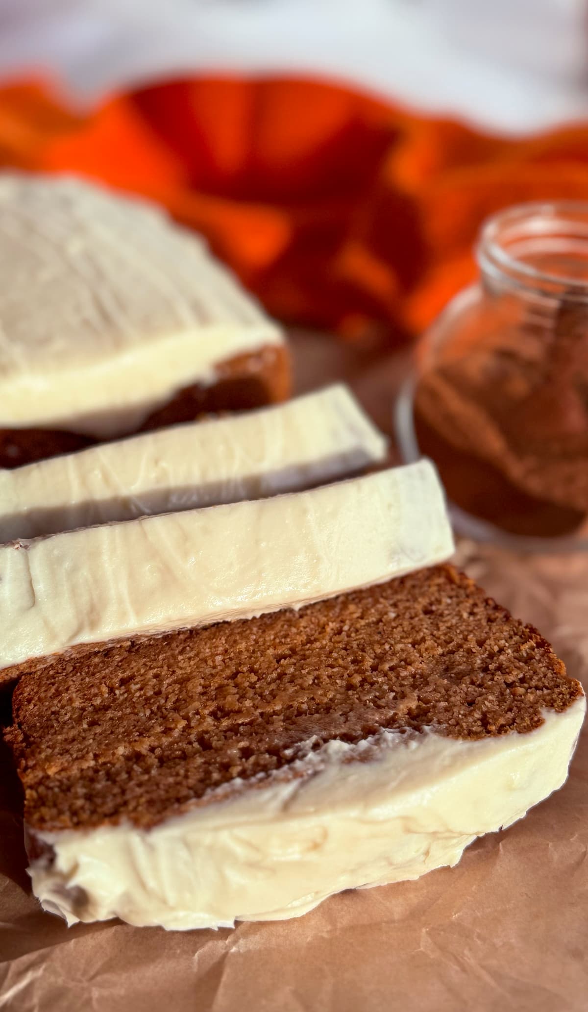 half sliced pumpkin bread with cream cheese frosting next to a jar of pumpkin spice.