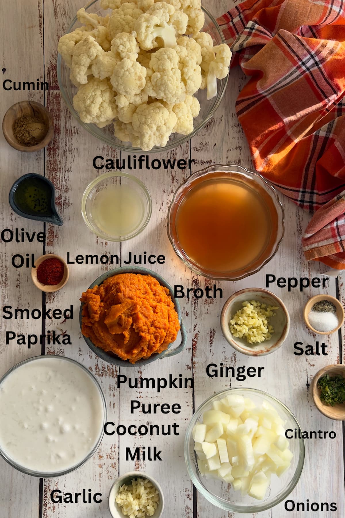 ingredients for cauliflower pumpkin soup set out in different bowls - cauliflower, cumin, smoked paprika, olive oil, broth, salt, pepper, lemon juice, ginger, garlic, onions, cilantro, pumpkin puree, coconut milk.