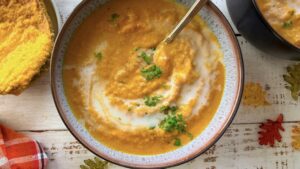 close up of a bowl of pumpkin and cauliflower soup with a swirl of coconut cream and chopped cilantro on top.
