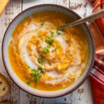 two bowls of cauliflower and pumpkin soup with chopped cilantro and a swirl of coconut cream on top. plate with a dirty soup spoon next to it.