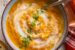 two bowls of cauliflower and pumpkin soup with chopped cilantro and a swirl of coconut cream on top. plate with a dirty soup spoon next to it.