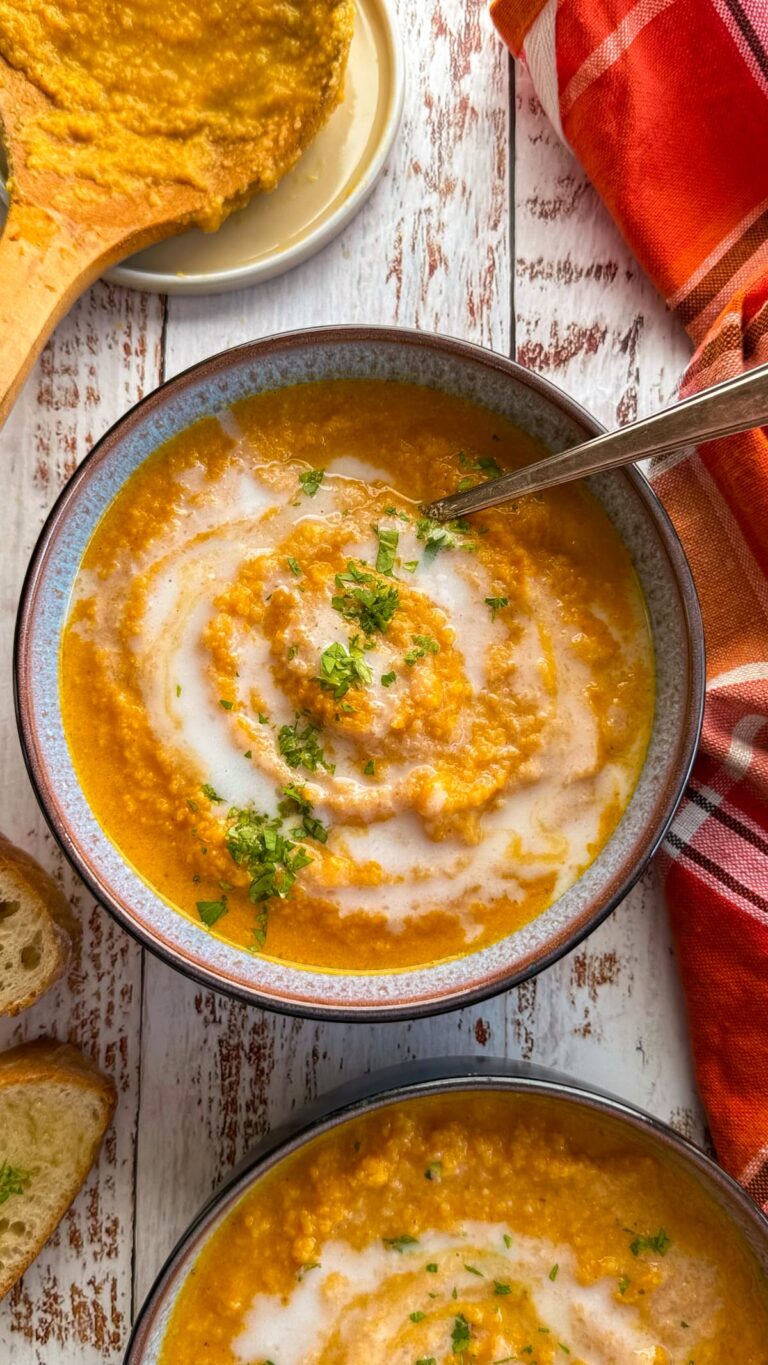 two bowls of cauliflower and pumpkin soup with chopped cilantro and a swirl of coconut cream on top. plate with a dirty soup spoon next to it.