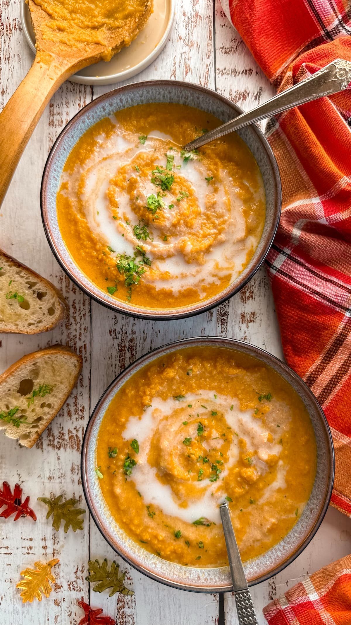 two bowls of cauliflower pumpkin soup with chopped cilantro and coconut milk on top. spoons in the bowl. plate with a dirty soup spoon and 2 pieces of garlic bread next to the soup bowls.
