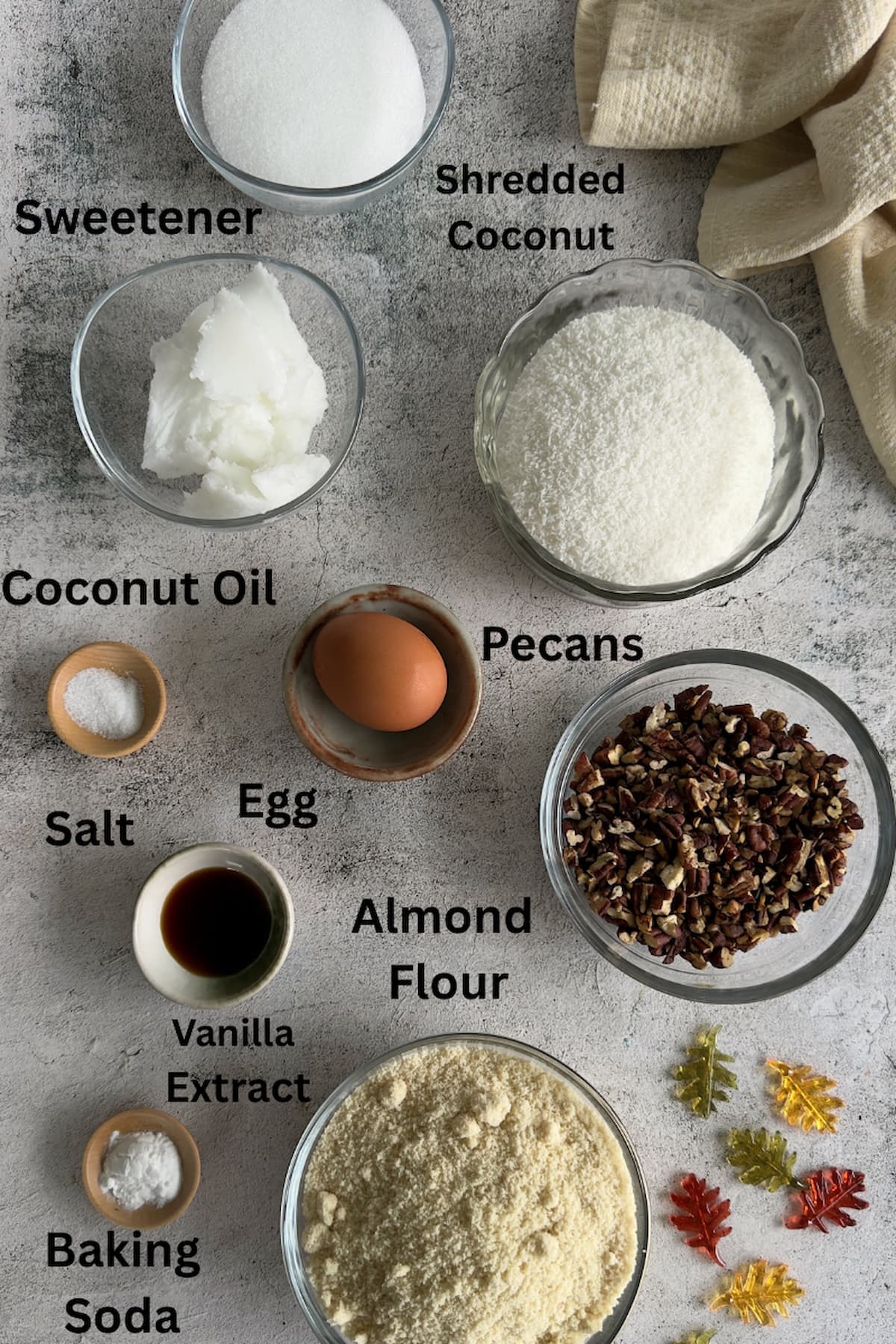 ingredients for coconut pecan cookies set out in separate bowls - coconut oil, sweetener, shredded coconut, egg, salt, pecans, baking soda, almond flour, vanilla extract.