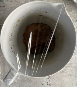 plastic wrap covering a bowl with a ball of brown cookie dough.