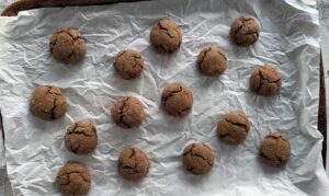 freshly baked brown gingerbread molasses cookies spread out on a parchment lined baking sheet.
