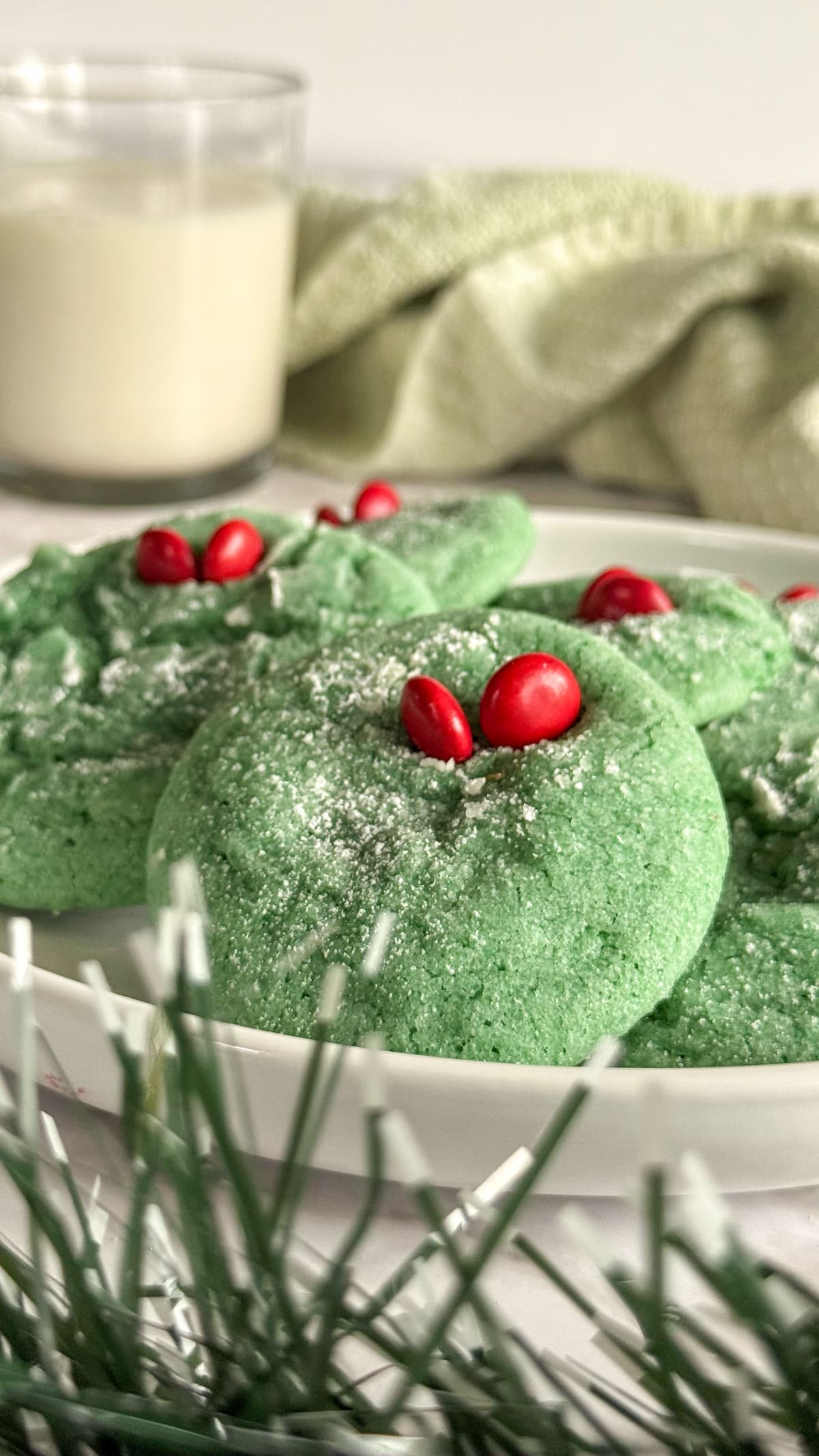 green grinch crinkle cookies on a white plate. glass of milk in the background.