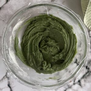 bowl of green cookie batter covered in siran wrap.