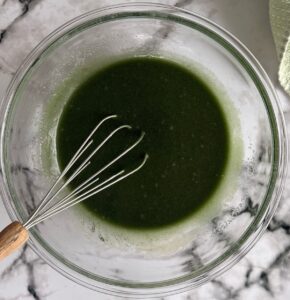 whisk in a bowl with dark green batter.