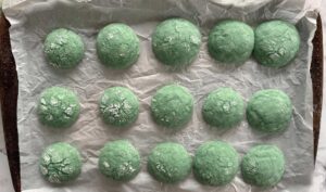 freshly baked green cookies topped with powdered sugar on a parchment lined baking sheet.