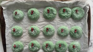 freshly baked grinch crinkle cookies with a red M&M heart and powdered sugar on a parchment lined baking sheet.