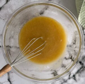 dark yellow liquid mixture in a clear bowl with a whisk.