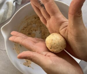 hands rolling a mini cheese ball over a white bowl.