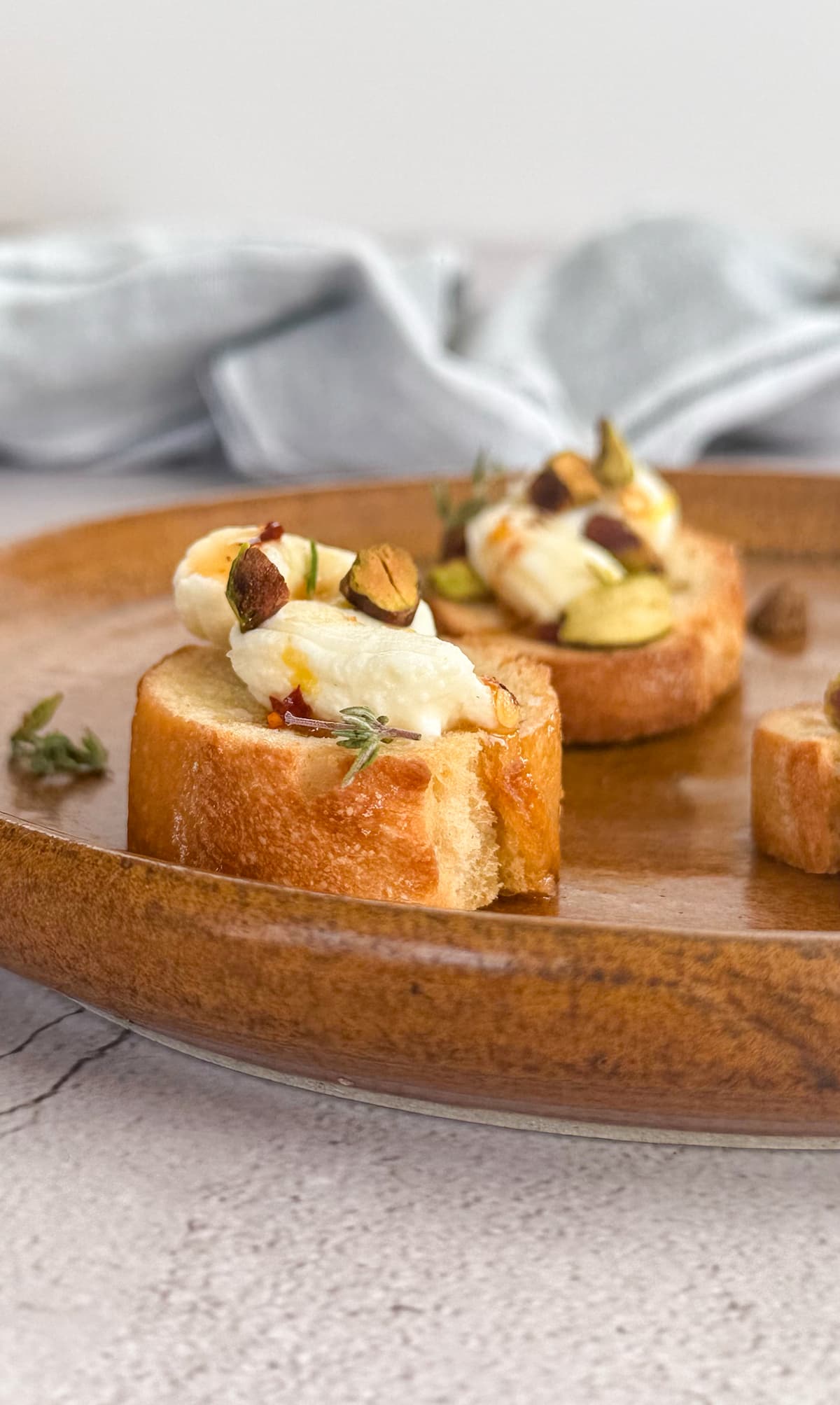 ricotta and hot honey crostini with chopped pistachios and thyme on a brown plate.