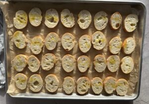 sliced baguette pieces drizzled with olive oil on a parchment lined baking sheet.
