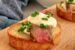 steak crostini with horseradish cream and chives on a board next to another crostini and a bowl of more horseradish cream.