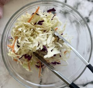 coleslaw in a bowl with tongs.