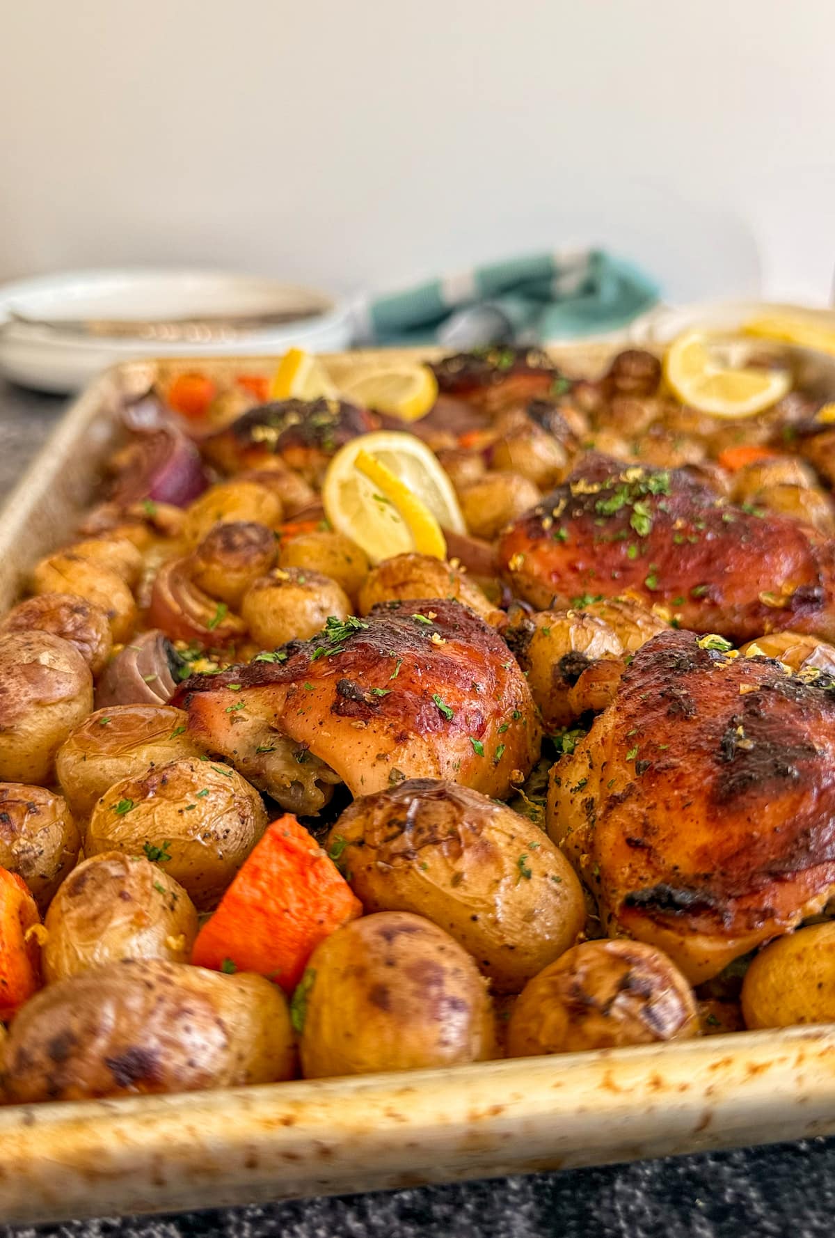 side view of chicken and lemon tray bake with potatoes, carrots, red onion, and parsley.