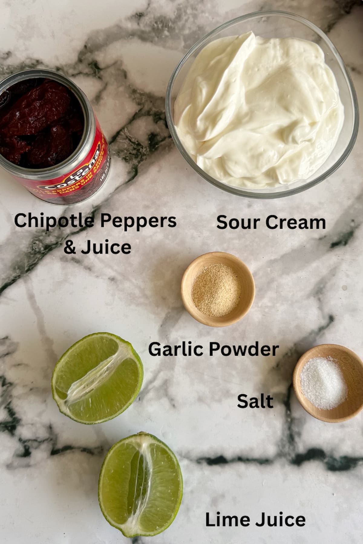 ingredients for chipotle sour cream laid out - halved lime, can of chipotle peppers in adobo, sour cream, salt, and garlic powder.