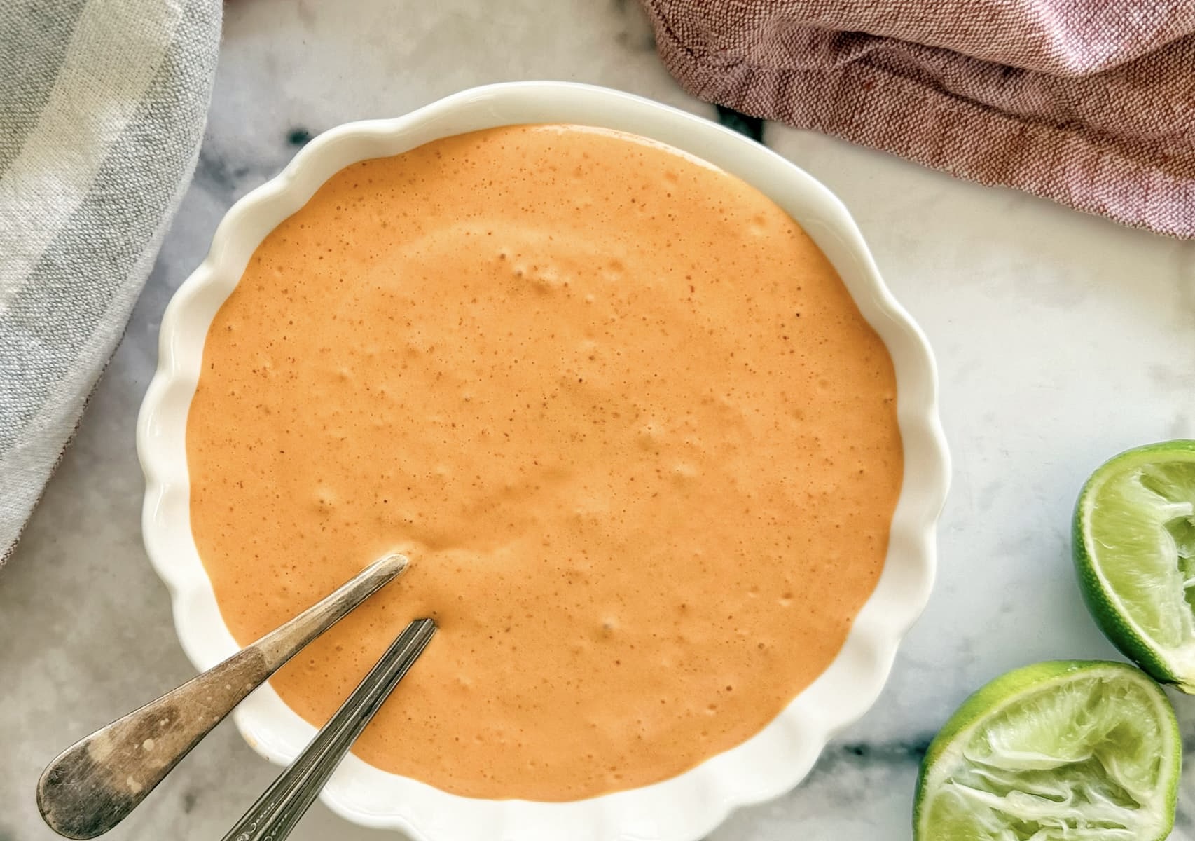 bowl of orange chipotle sour cream sauce with two spoons next to a halved lime.
