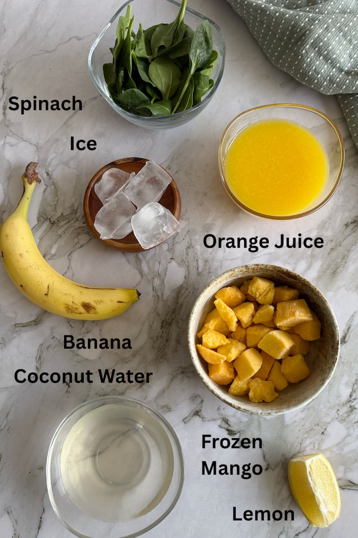 ingredients to make a green machine smoothie laid out in different bowls - spinach, orange juice, ice, frozen mango, coconut water, banana and lemon.