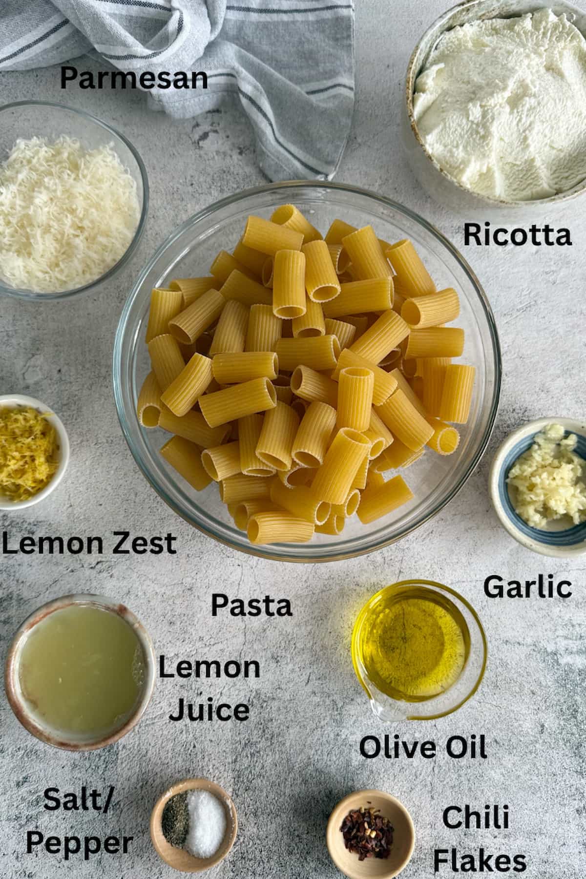 ingredients for one pot pasta with ricotta and lemon laid out in small bowls - parmesan, ricotta, pasta, lemon zest, olive oil, garlic, lemon juice, salt, pepper, and chili flakes.