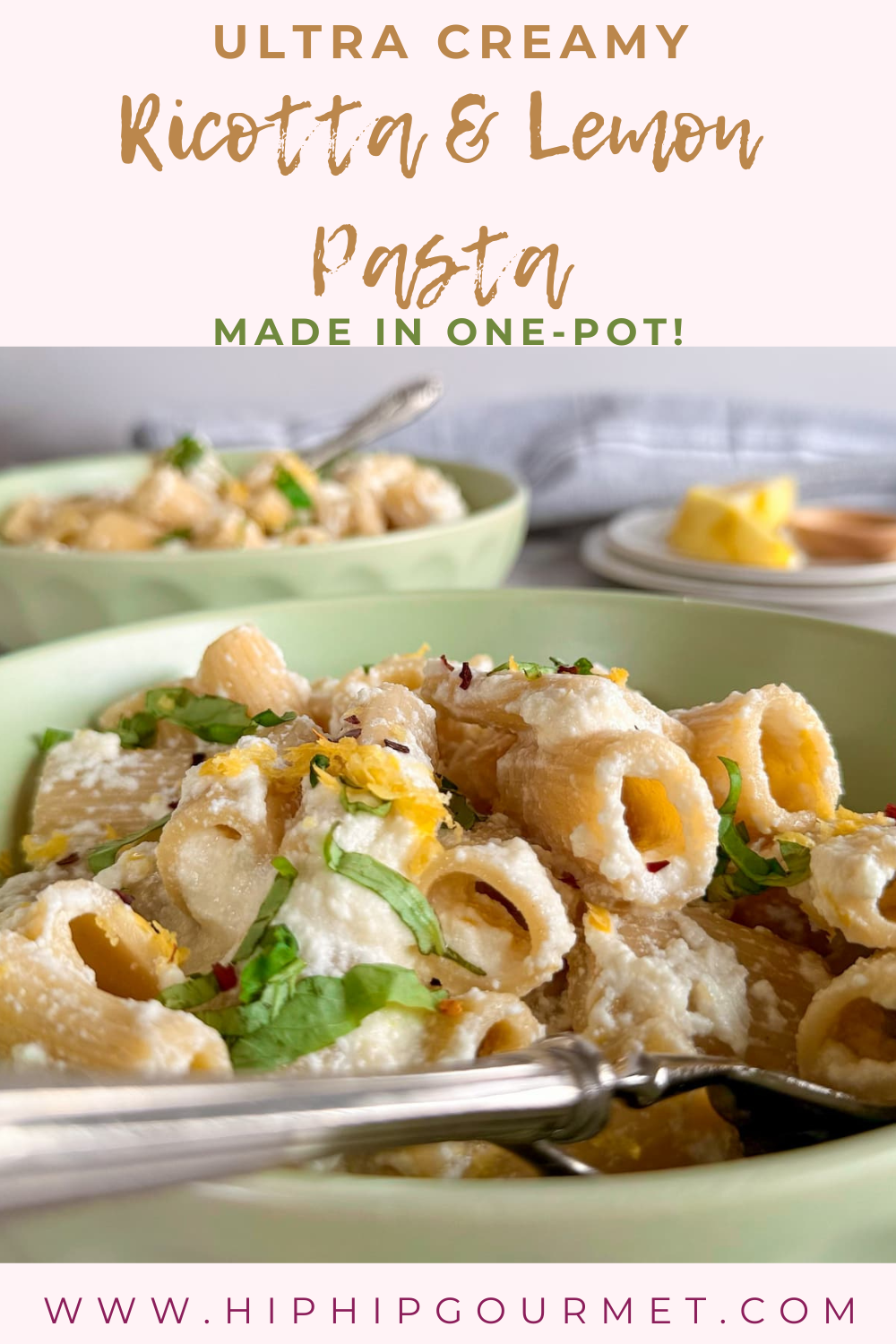 side view of creamy rigatoni in a bowl topped with lemon zest, ricotta, chili flakes, and chopped basil. Another bowl of pasta next to a couple plates of lemon in the background.