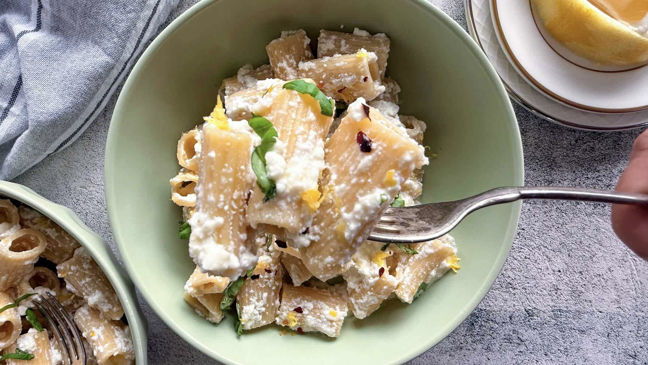 forkful of lemon ricotta pasta with fresh basil over a bowl with more.