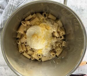 silver pot of rigatoni pasta topped with a dollop of ricotta, parmesan, and lemon zest.