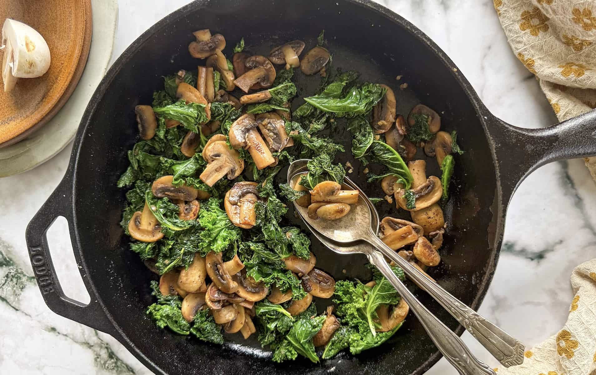 sauteed kale and mushrooms in a cast iron skillet with two spoons.
