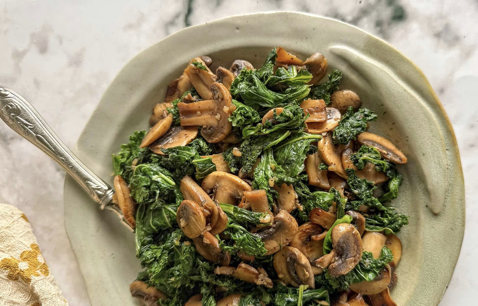 sauteed kale and mushrooms on a plate with a spoon.