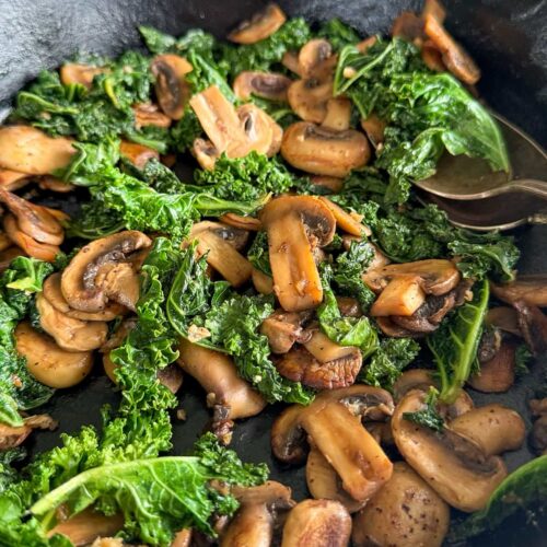 cast iron skillet with cooked sliced mushrooms and kale.