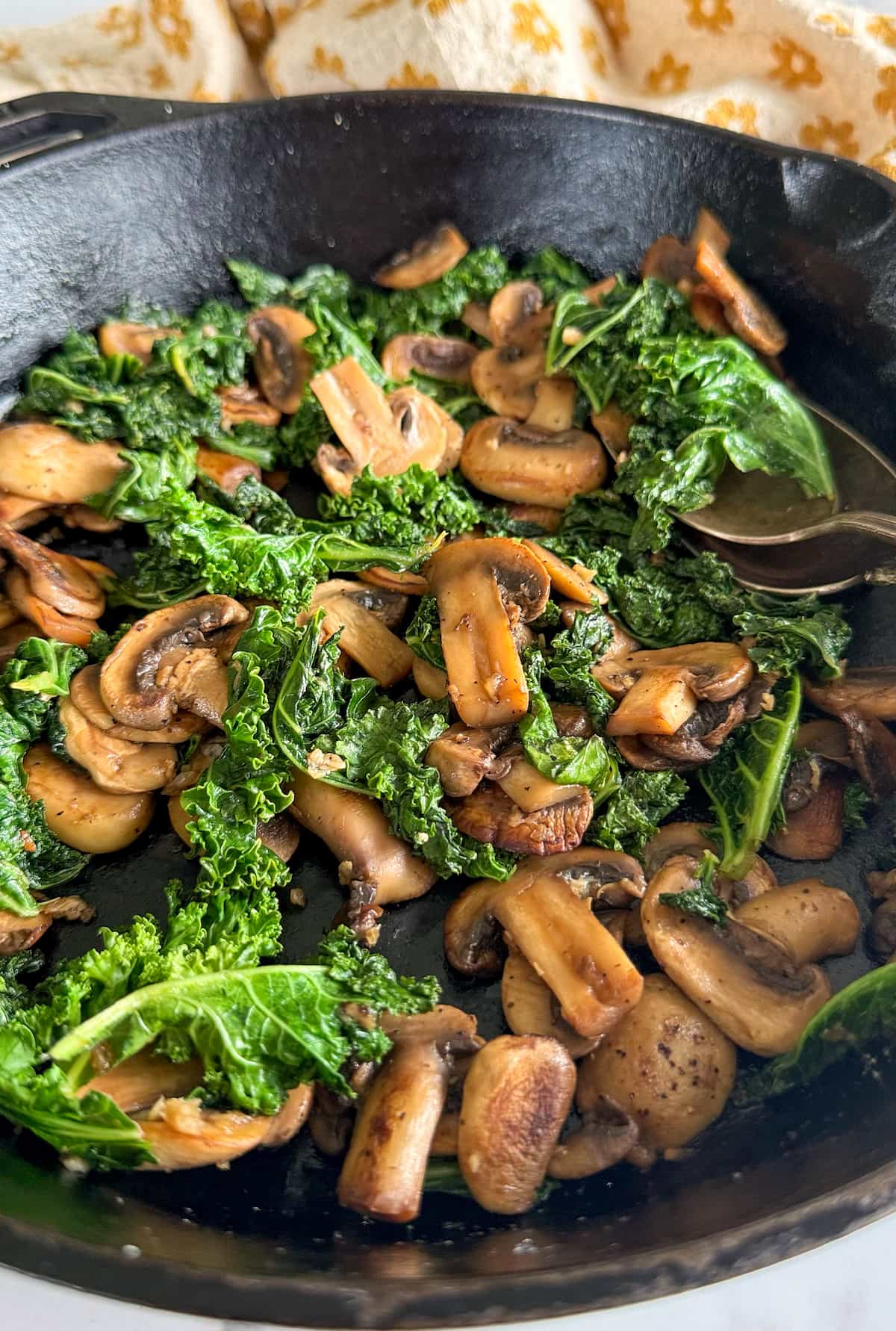 cast iron skillet with cooked sliced mushrooms and kale.