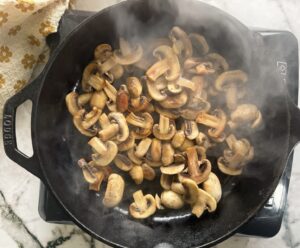 browned sliced mushrooms steaming in a cast iron skillet.