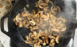 sliced browning mushrooms with minced garlic steaming in a cast iron skillet.