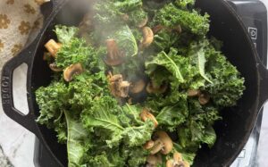 torn pieces of kale and sliced mushrooms cooking in a cast iron skillet.