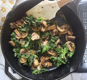 sauteed kale and mushrooms in a cast iron skillet with a rubber spatula.