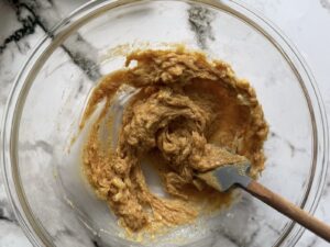 peanut butter and mashed banana mixture in a glass bowl with a small rubber spatula.