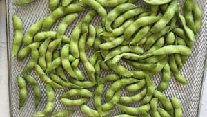 frozen salted edamame spread out on an air fryer tray.