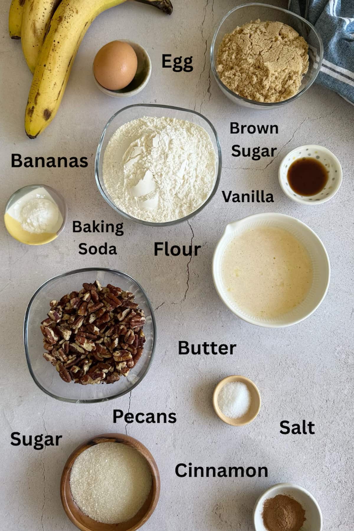 ingredients for banana pecan muffins laid out in separate bowls - sugar, pecans, cinnamon, salt, baking soda, vanilla, butter, egg, bananas, and brown sugar.