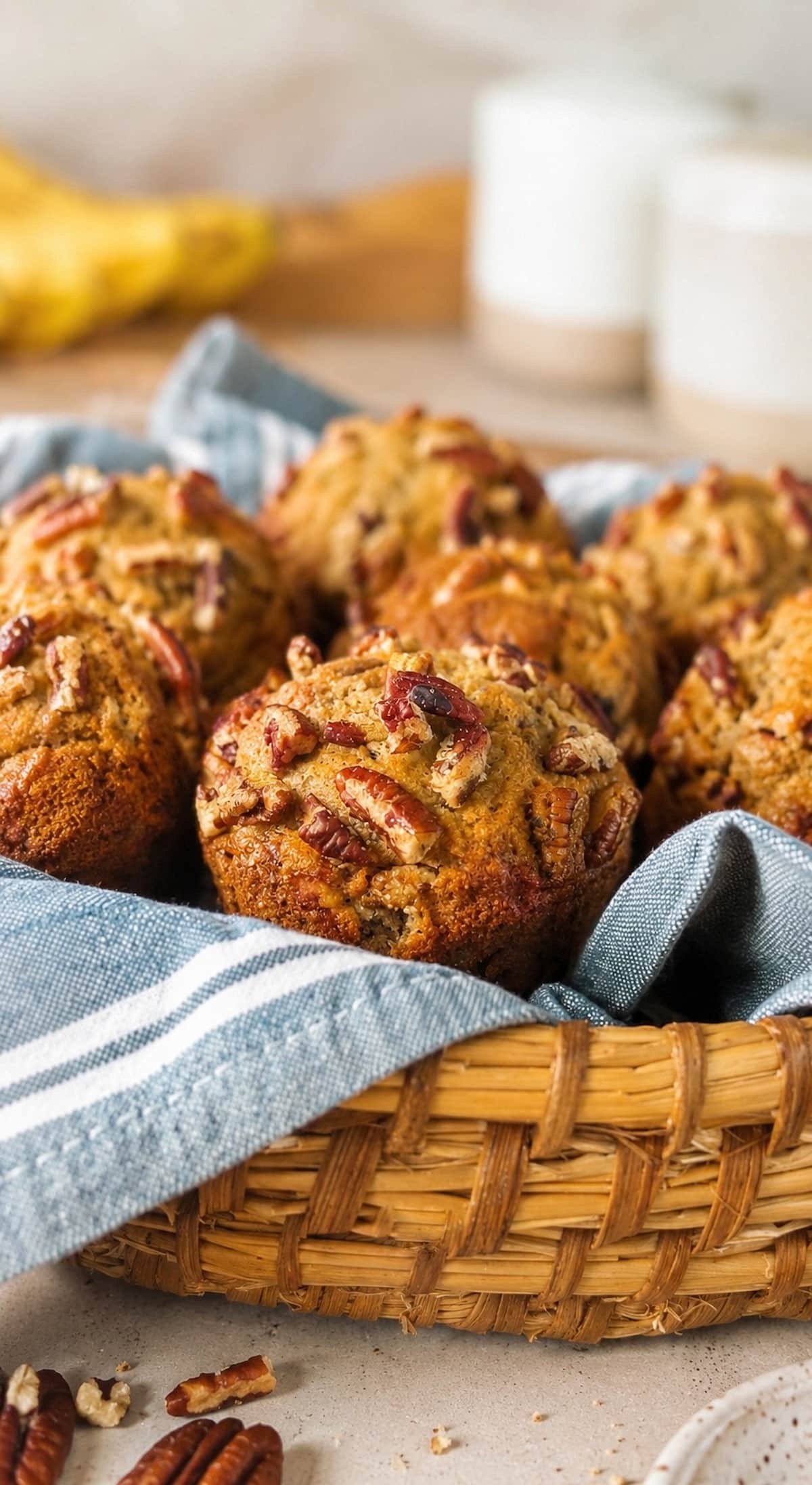 close up photo of banana pecan muffins in a woven basket lined with a blue striped kitchen towel.