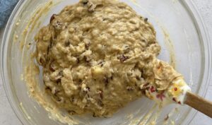 banana pecan muffin batter with chopped pecans in a glass bowl with a flowered rubber spatula.
