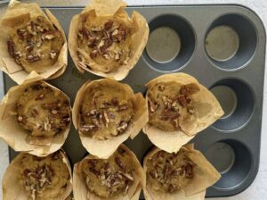 8 unbaked banana pecan muffins in a dark muffin tin, with 4 empty slots.