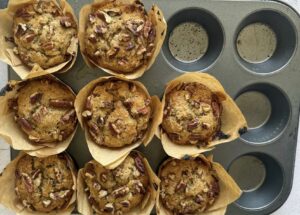 8 freshly baked banana pecan muffins in a dark muffin tin, with 4 empty slots.