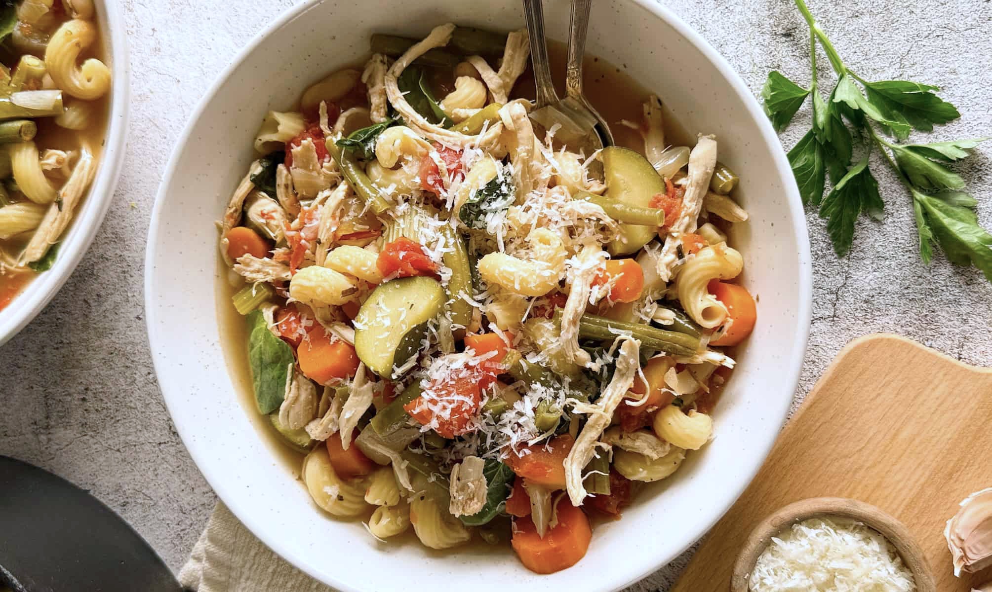 bowl of chicken minestrone soup loaded with zucchini, beans, carrots, tomatoes, pasta, shredded chicken, and parmesan cheese.