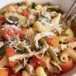 side view of a bowl of chicken minestrone soup loaded with chopped veggies, beans, pasta, and parmesan cheese.