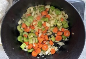 black cast iron pot with chopped celery, carrots, and white onions.